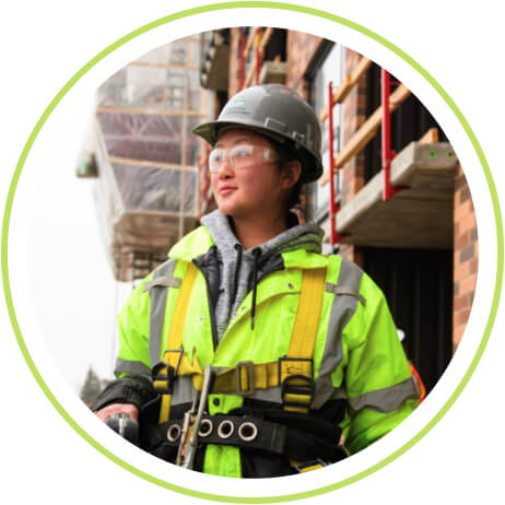 A construction worker in safety gear stands in front of a building site, looking into the distance, embodying the dedication that shapes our built environment.