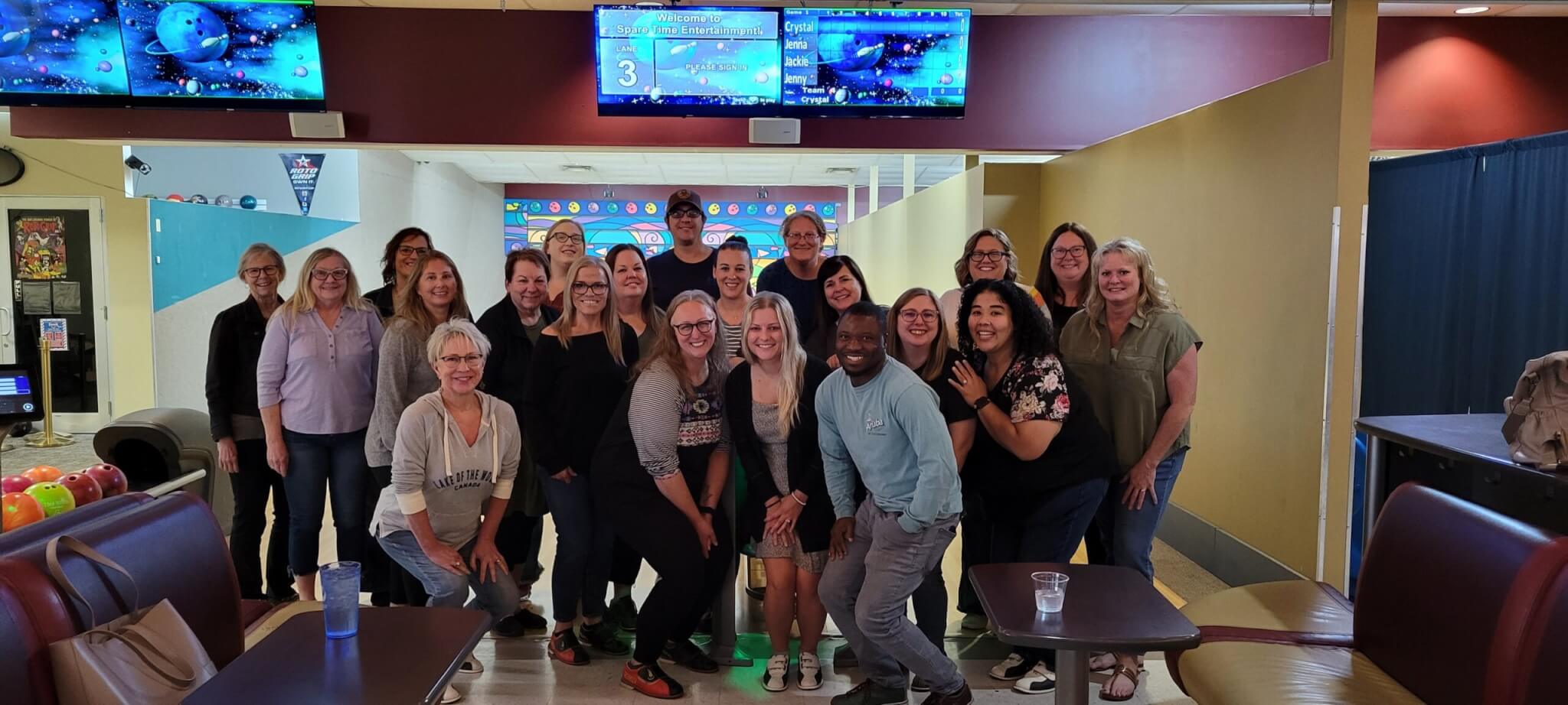 A group of people smiling and posing together inside a bowling alley.