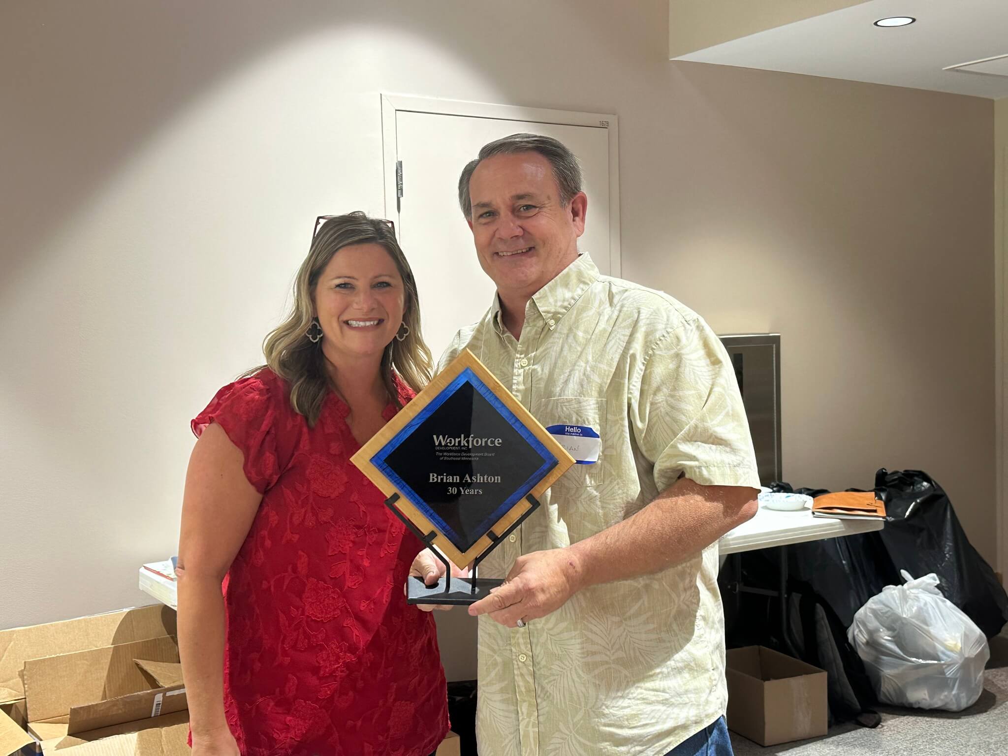 Two people smiling, one holding a Workforce award for 30 years, standing in an indoor setting.