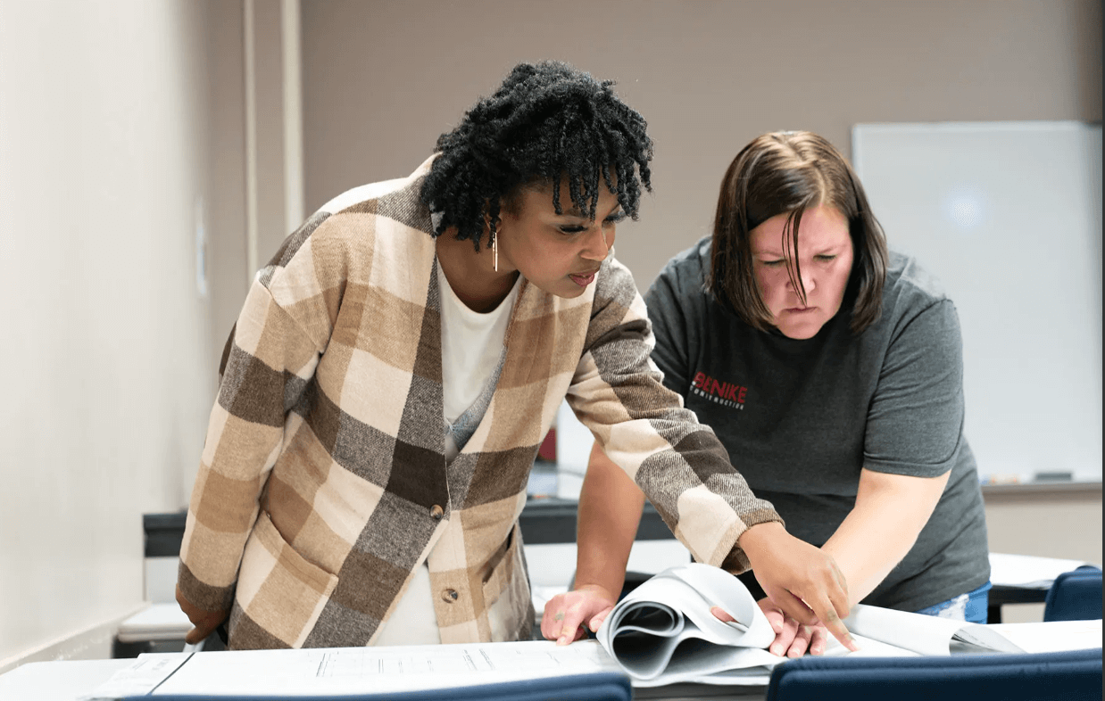 Two women stand and look at papers on a table, collaborating in a classroom or office setting as part of the Bridges to Careers program.