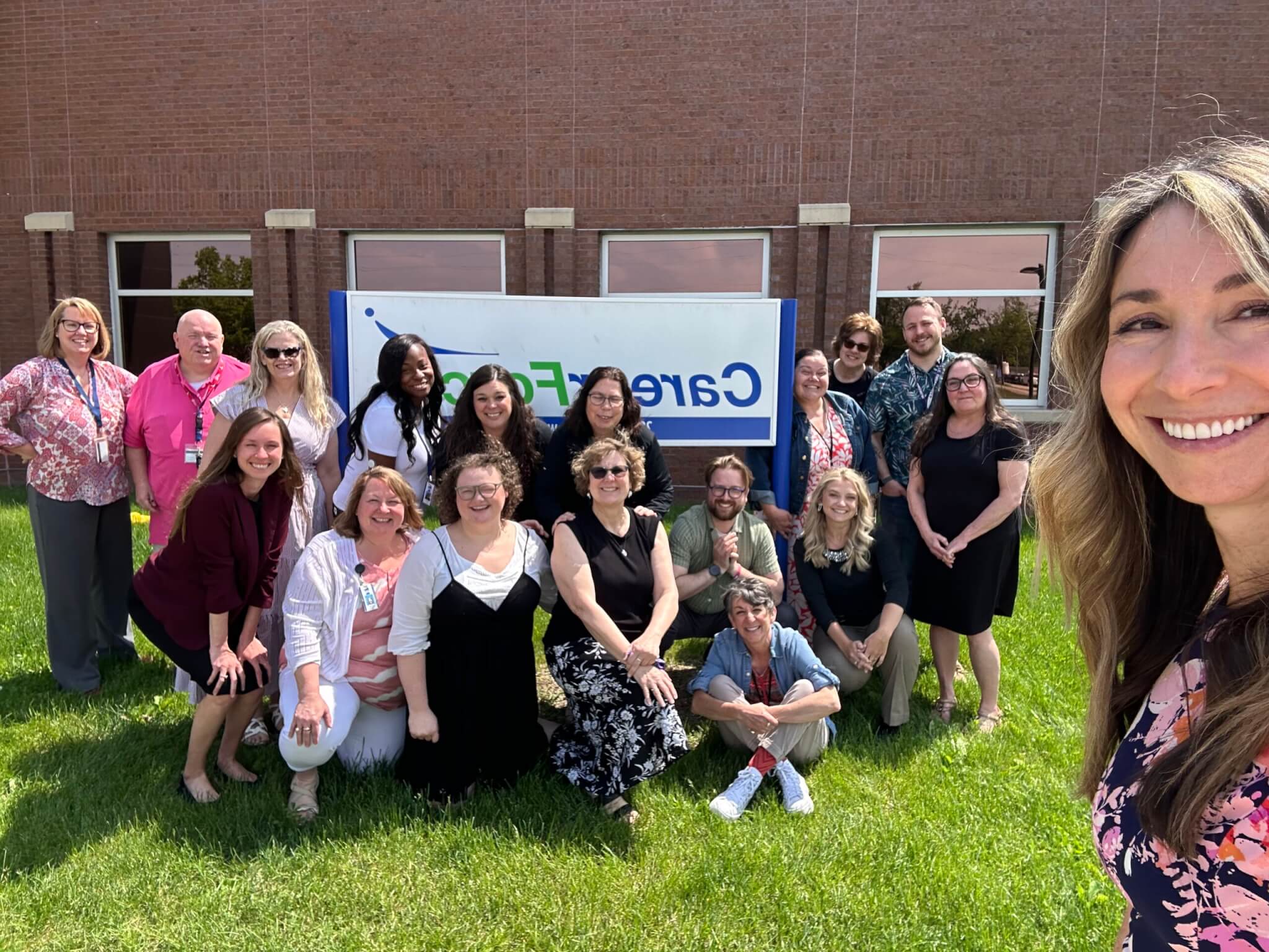 A group of people smiling and posing for a photo outside on grass in front of a brick building and a CareNet sign.