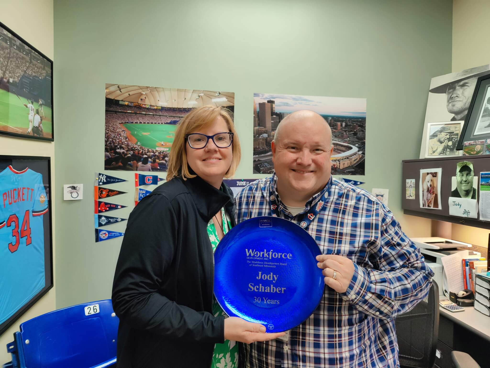 Two people smiling in an office, holding a blue 30-year service award plate for Jody Schaber.