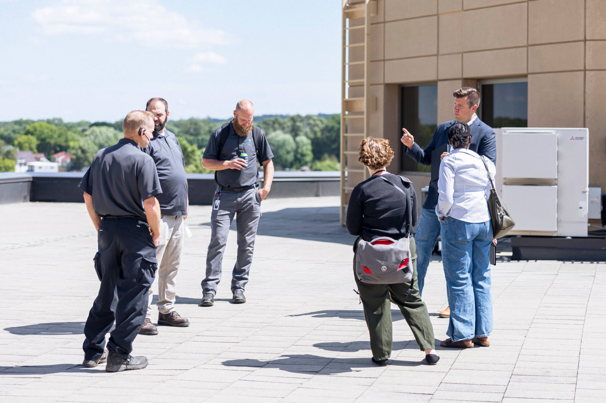 Six people stand in a circle talking on a sunny rooftop, connecting over Bridges to Careers, with trees and buildings in the background.