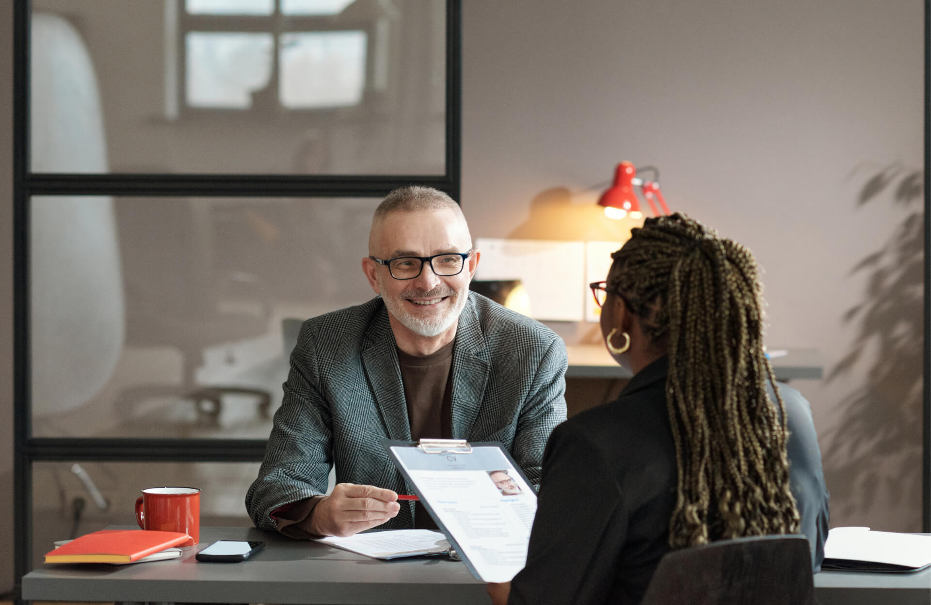 Two people sit across a desk in an office, having a conversation during a job interview, discussing Labor Market Information and how it relates to the position.