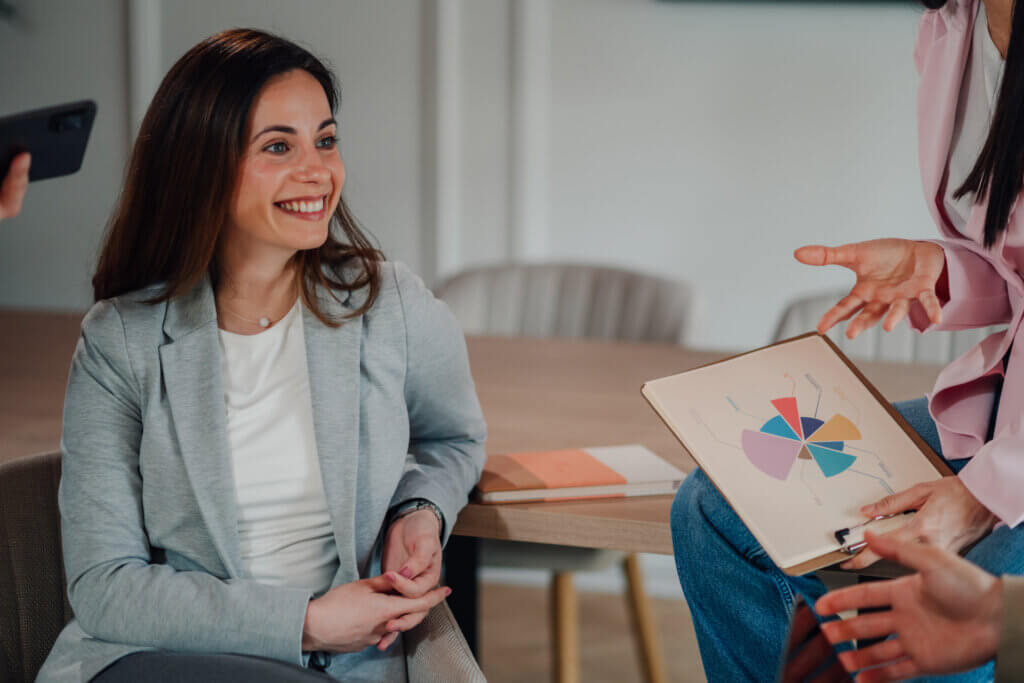 A woman smiling during a Bridges to Careers meeting while others discuss a colorful pie chart on a clipboard.