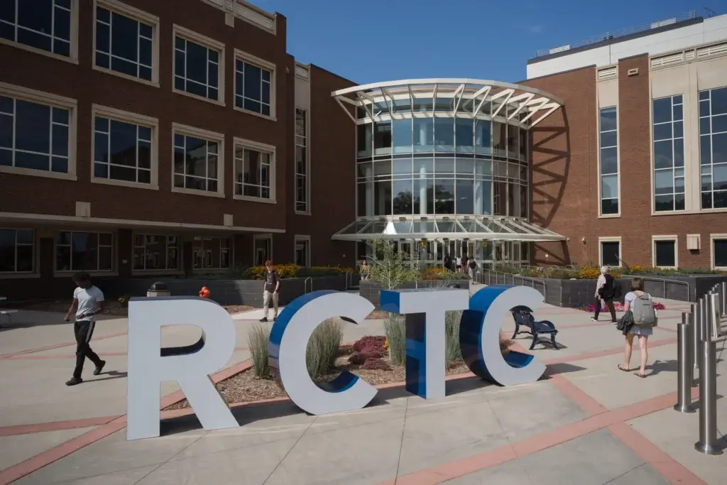 Large RCTC letters stand proudly in front of a modern brick campus building, where students walk around, exploring new opportunities and building Bridges to Careers.