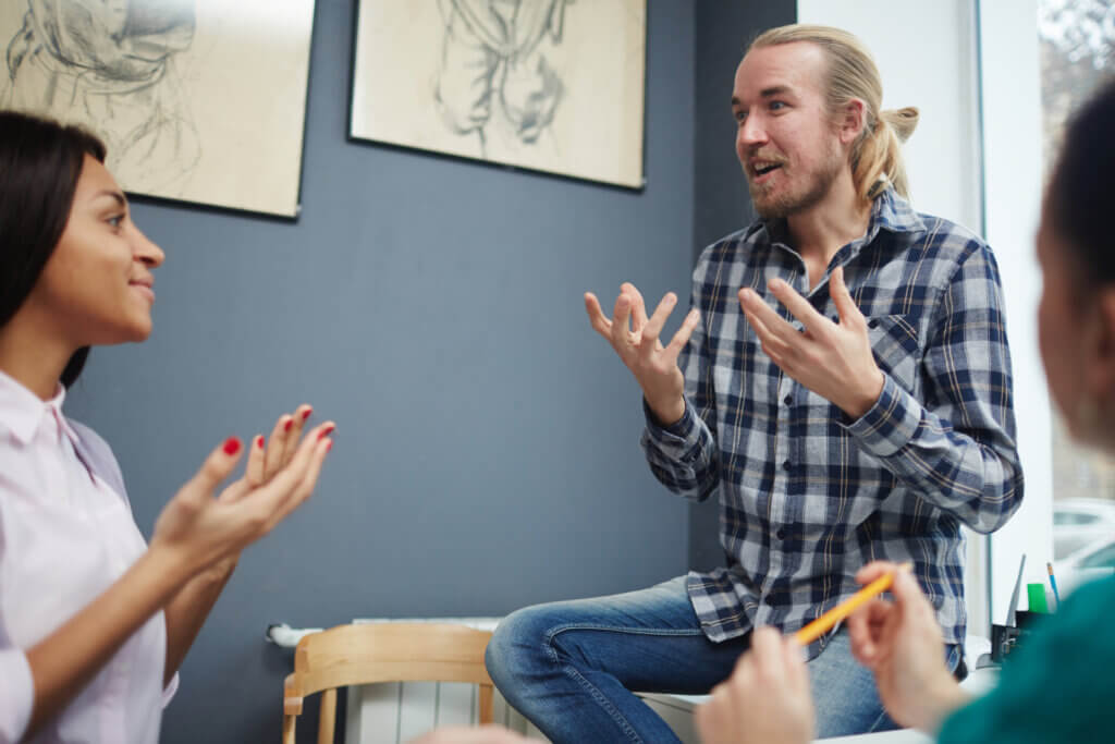 Man in plaid shirt talking animatedly to two women in a casual indoor setting with art on the walls, possibly discussing career planning.