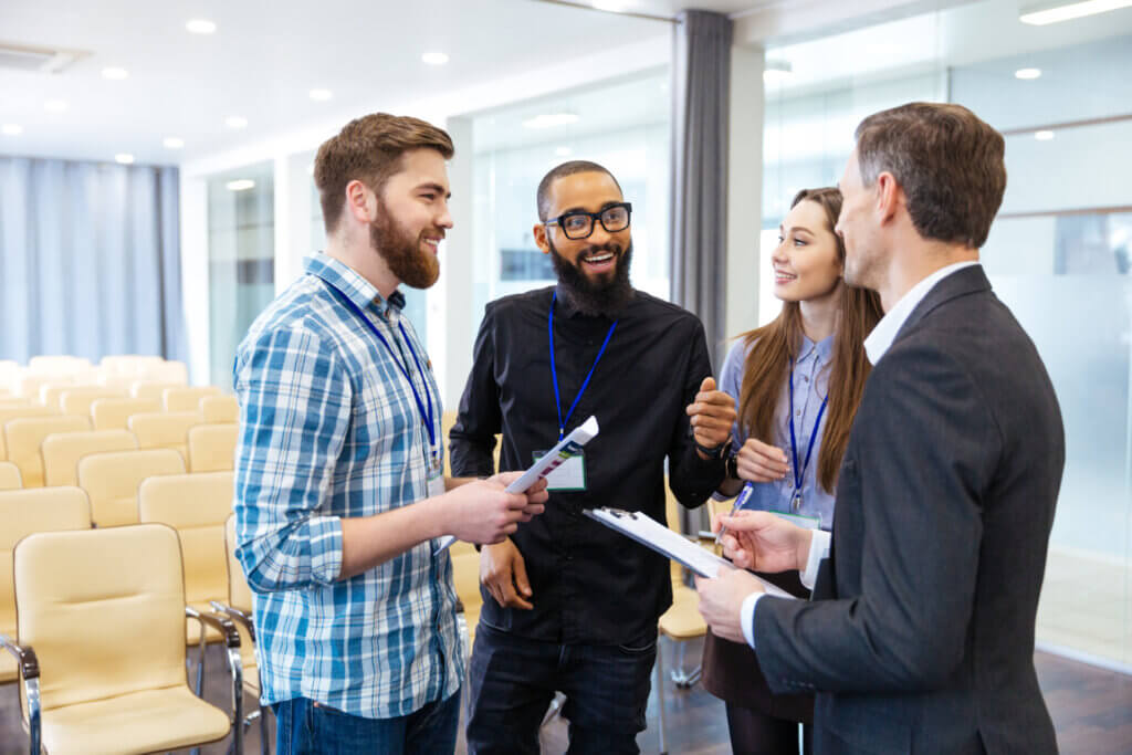 Four people with name badges talking and smiling in an empty conference room with chairs and glass walls during staff training.