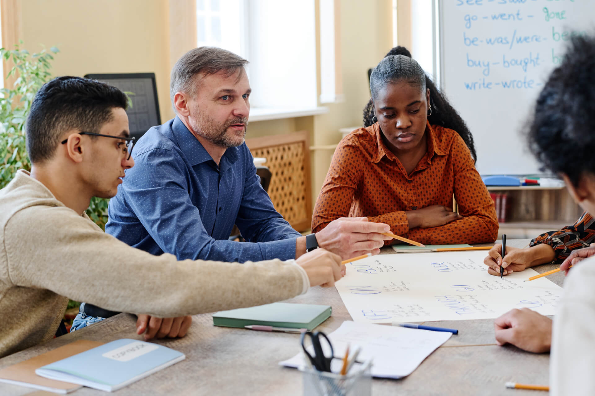 Four people sit around a table, discussing notes and writing on a large sheet of paper together.