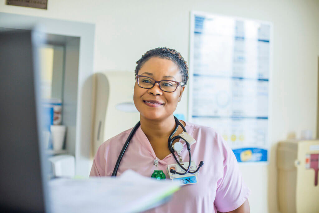 Smiling nurse in scrubs with a stethoscope around her neck, standing in a medical office, representing the Bridges to Careers pathway in healthcare.