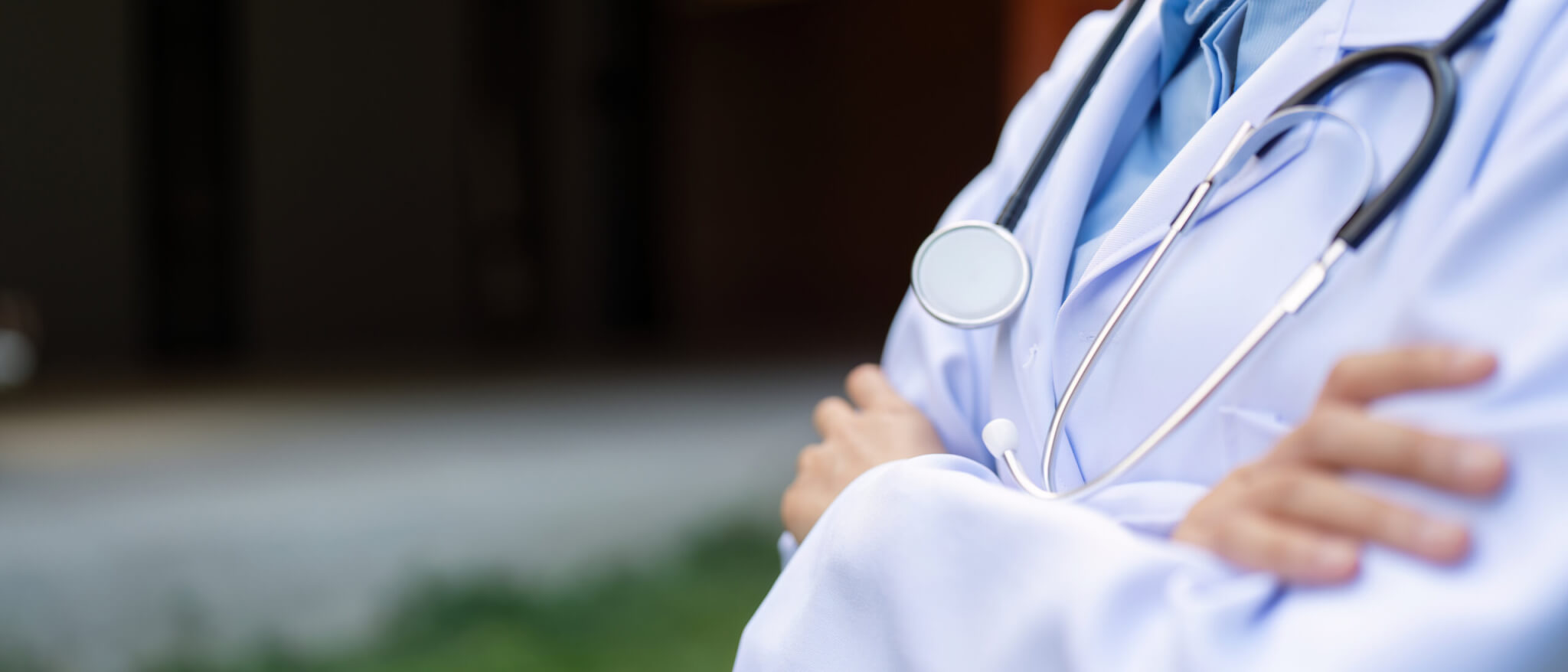 A doctor in a white coat with a stethoscope stands with arms crossed, representing the professionalism found in rewarding healthcare careers, background blurred.