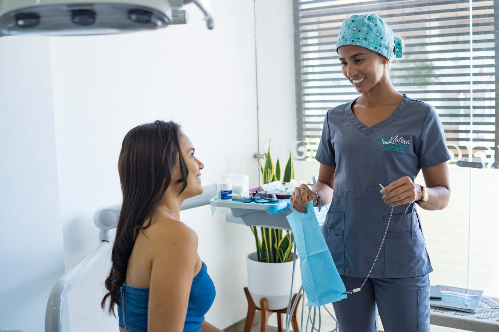 A dentist in scrubs smiles at a seated patient in a dental office, holding a dental bib—a welcoming scene for those exploring healthcare careers or seeking rewarding healthcare jobs.
