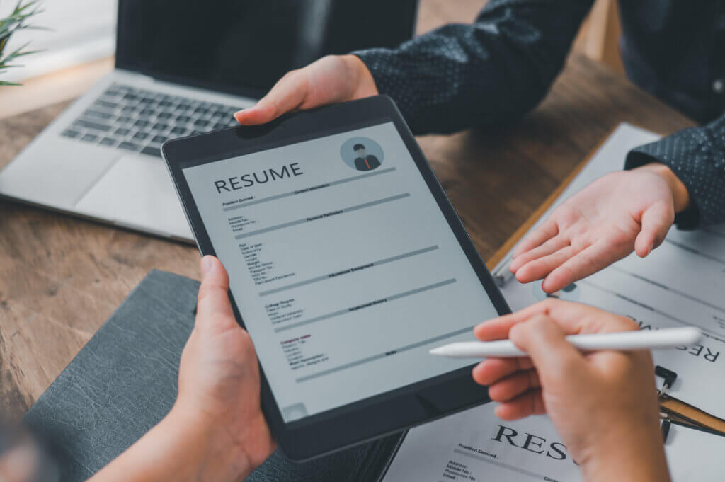 Two people review a digital resume on a tablet, surrounded by a laptop and papers—focusing on career skills and job readiness.