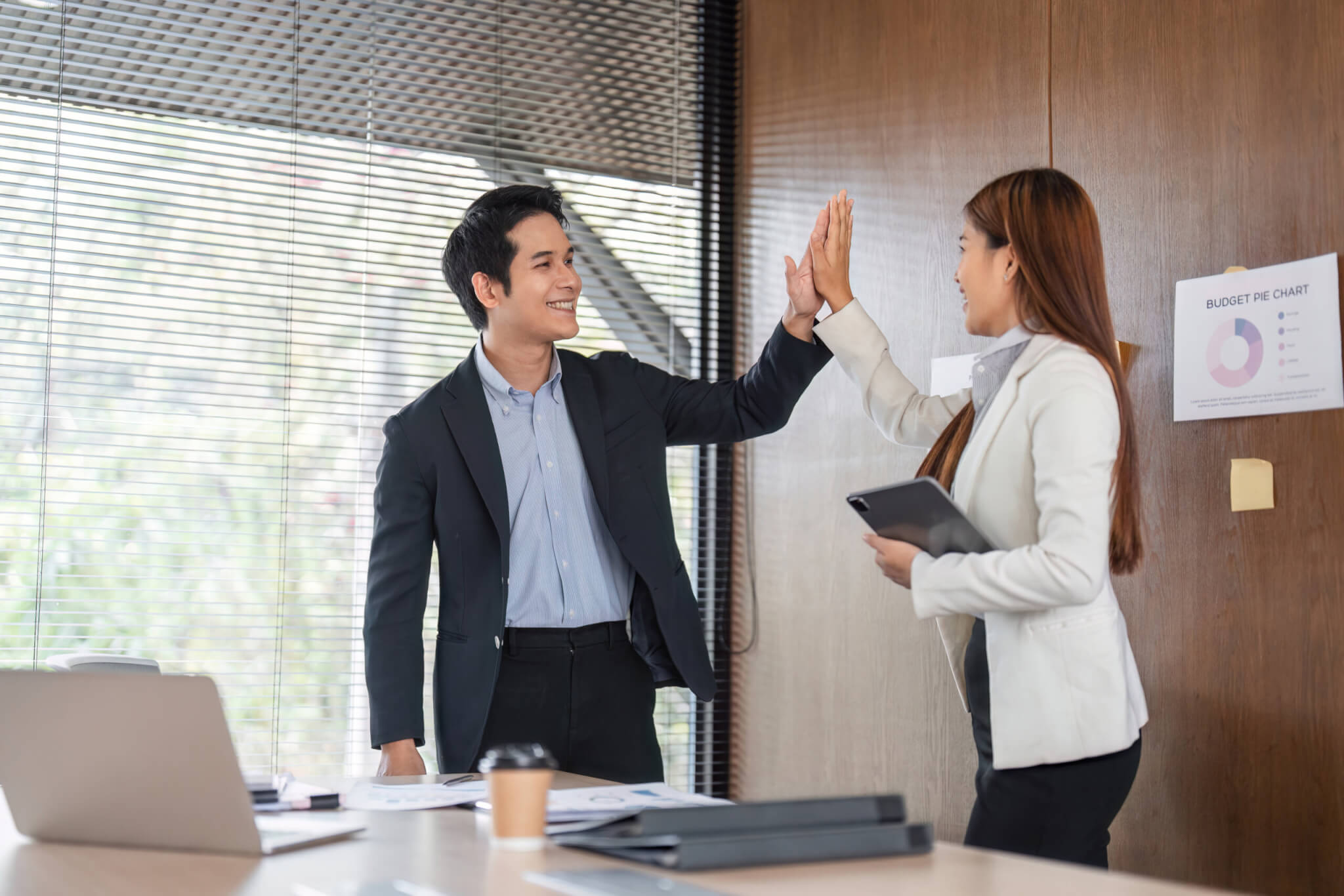 Two colleagues in business attire smiling and giving a high five in a modern office setting, celebrating their success through Bridges to Careers.