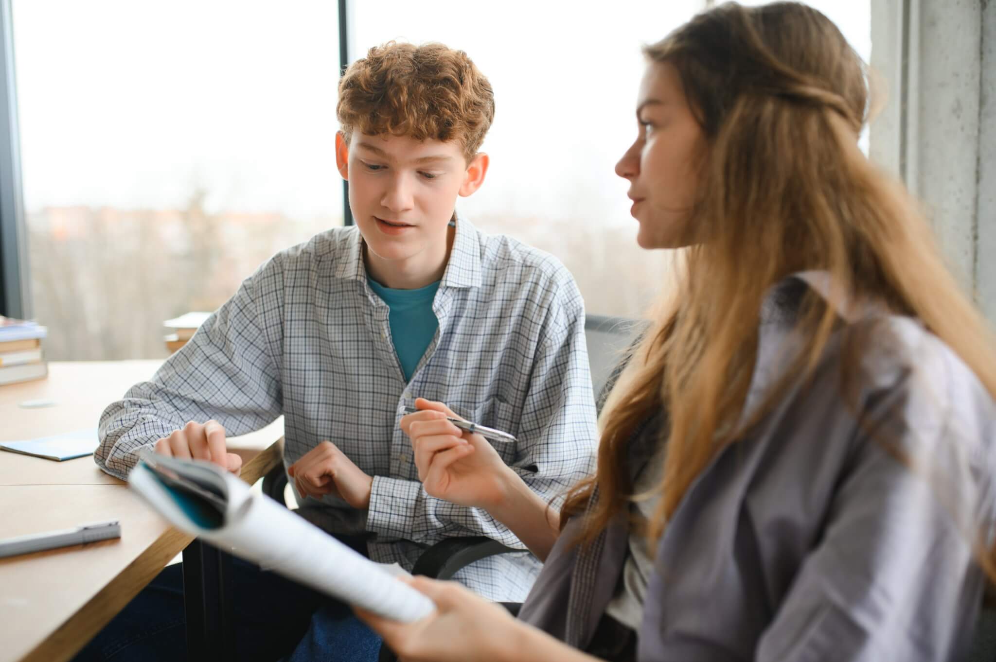 students sit at shared desk making notes studying together at university.