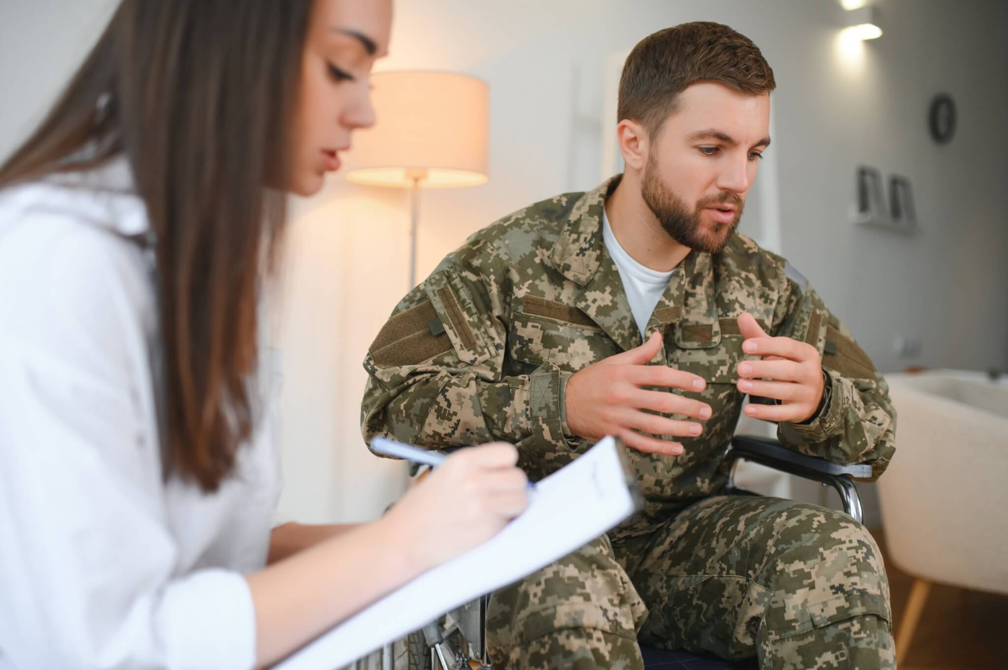 A soldier in a wheelchair discusses his experiences with a woman taking notes on a clipboard, highlighting the importance of Veteran Services.
